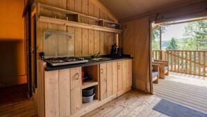 Une cuisine rustique, aménagée dans une cabane en bois, avec une cuisinière à gaz, un évier et des étagères au-dessus.