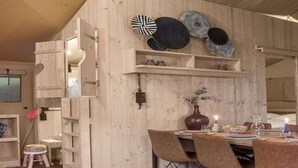 Un intérieur en bois comprenant un coin repas avec une table dressée pour quatre personnes, un vase rempli de fleurs et des assiettes décoratives disposées sur des étagères.