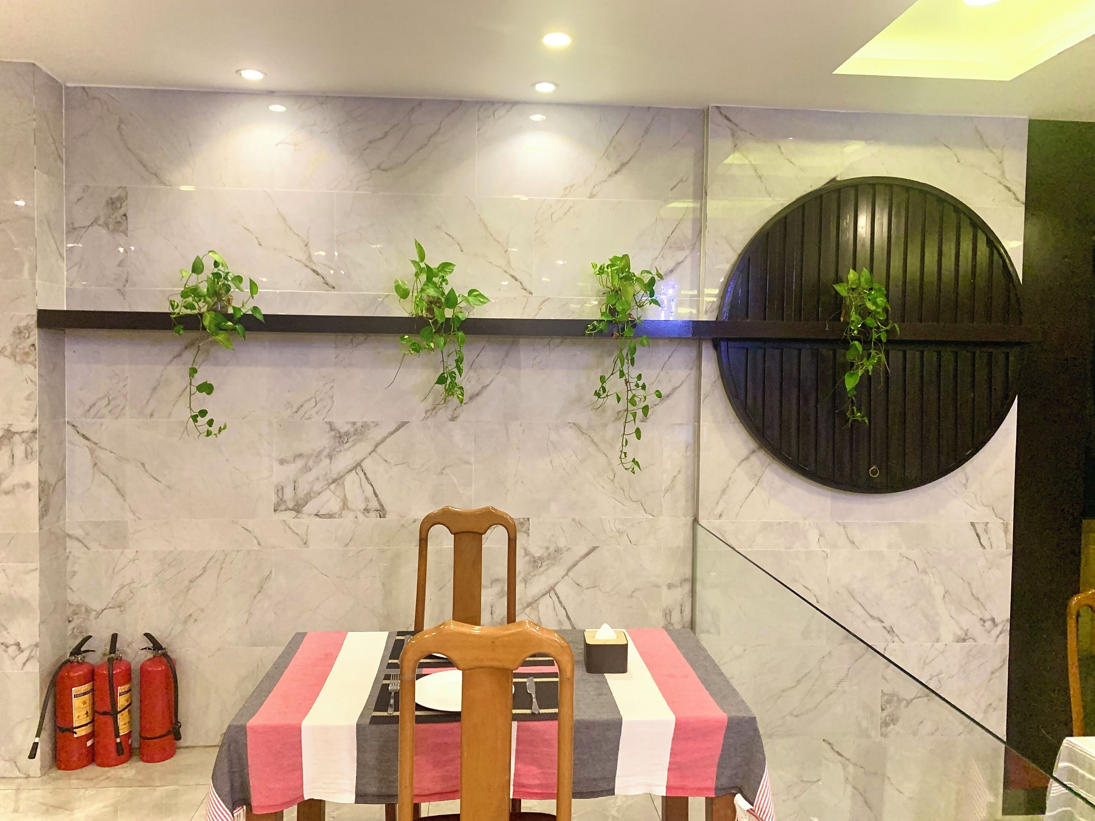 A dining area with a marble wall, a wooden chair, a table with a striped tablecloth, and fire extinguishers.