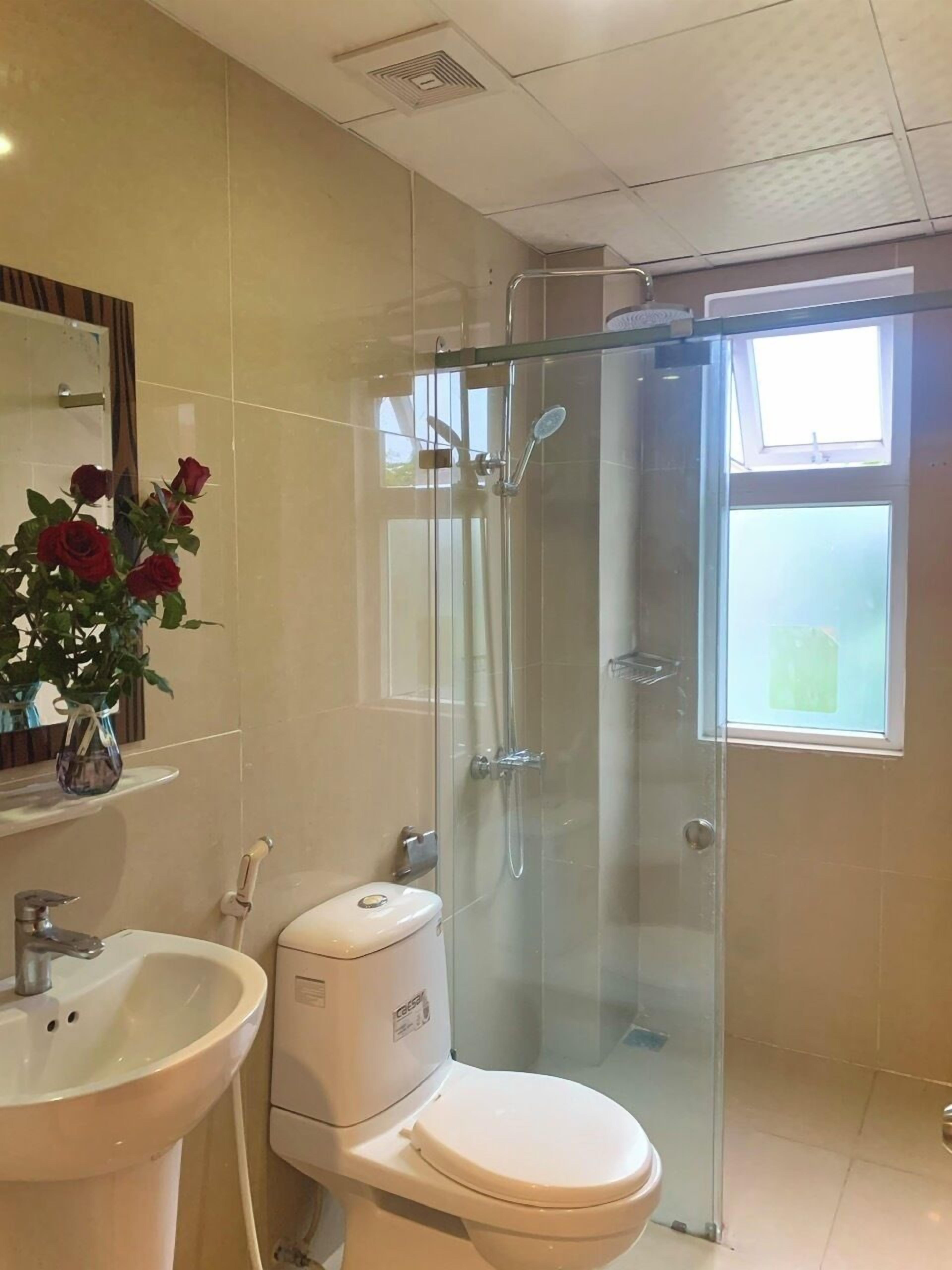 A bathroom with a glass-enclosed shower, a white toilet, and a sink with a vase of red roses.