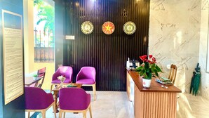 A reception area with a wooden reception desk, purple chairs, and a dark wall with decorative plates. - Aman Riverside Hotel (Da Nang)