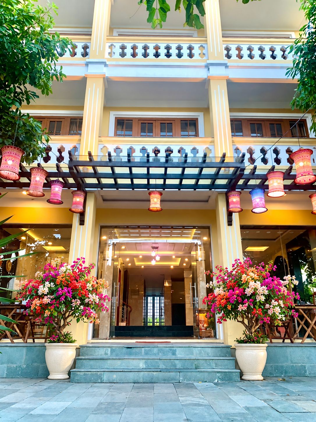 A hotel entrance with a covered porch, potted plants, and a staircase leading to the entrance.