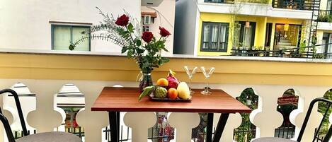 A balcony with a table set with fruits and flowers, two chairs, and a decorative metal railing.