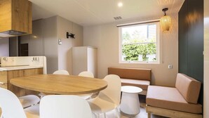 Una cocina moderna con una mesa de madera y sillas blancas, horno empotrado y un ventanal con vistas a la vegetación.