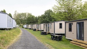 Una hilera de casas móviles con zonas de estar al aire libre, un camino de grava y árboles al fondo.