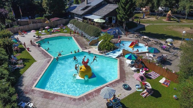 Una amplia piscina al aire libre con múltiples carriles y un tobogán acuático, rodeada de tumbonas y sombrillas.