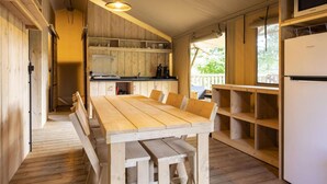 A wooden interior with a central dining table, a kitchen area with cabinets, and a refrigerator.