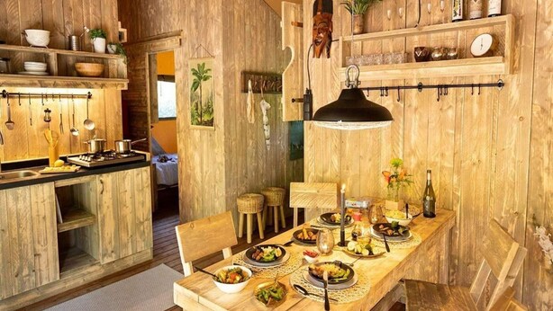 Un intérieur rustique avec des éléments en bois, notamment une table à manger dressée pour un repas, des armoires en bois et un luminaire suspendu.