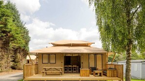 Een houten chalet met een overdekte veranda, een eettafel en een bank.