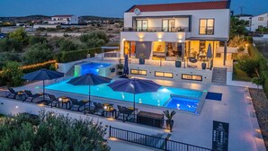 A modern two-story house with a swimming pool, outdoor seating, and a well-lit patio area.