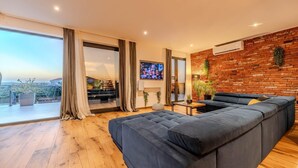 A modern living room with a large sectional sofa, a flat-screen TV, and a brick wall.