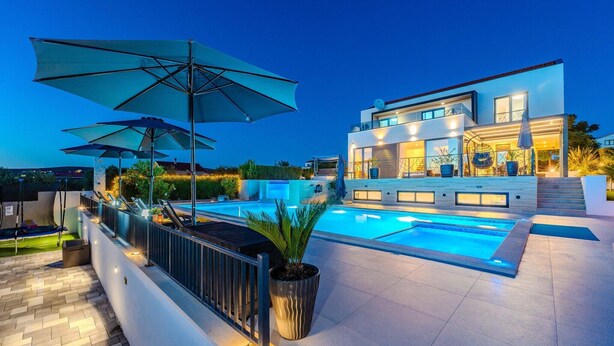 A modern poolside area with umbrellas, a pool, and a two-story building with large windows.