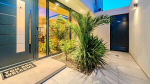 A modern building entrance with a glass door, a welcome mat, and a small garden area with plants.
