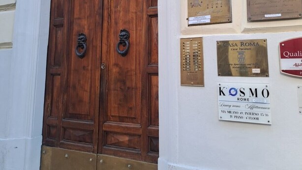 A double wooden door with brass knockers, a plaque reading "CASA ROMA", and a sign for "KOSMO ROME" with amenities listed. - The Five Oscars Inn (Rome)