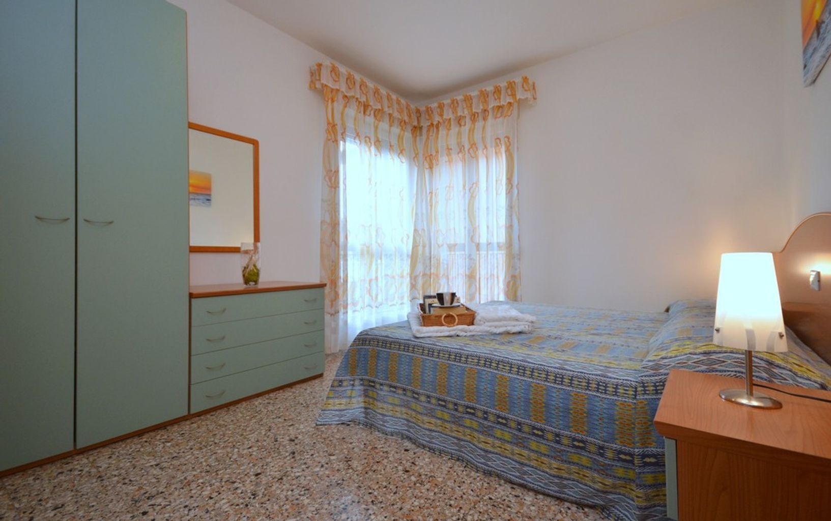 Un dormitorio con cama, mesita de noche, cómoda y ventana con cortinas.