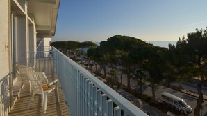 A balcony with two white plastic chairs and a small table, overlooking a street with parked cars and trees. - Beachside gem by Beahost Rentals (Lignano Sabbiadoro)