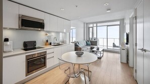 A modern kitchen with a built-in microwave, a dining area with a round table and chairs, and a sofa in a bright room with large windows. - DT Views | AC | Pullout Couch | Mins to Saddledome (Calgary)