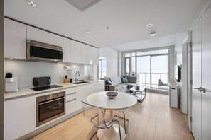 Una cucina moderna con forno a microonde integrato, un'area pranzo con tavolo rotondo e sedie, e un divano in una stanza luminosa con ampie finestre.