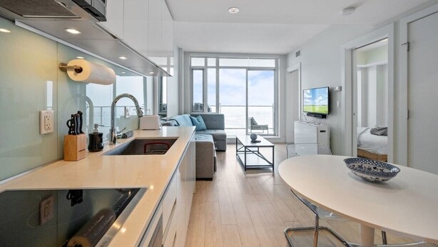 A modern kitchen with a built-in oven, a sink, and a dining area with a round table and chairs. - DT Views | AC | Pullout Couch | Mins to Saddledome (Calgary)