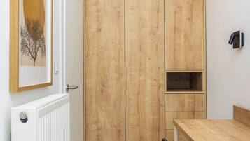 A room with a wooden wardrobe, a white radiator, a framed picture, a wooden table, and a black chair.