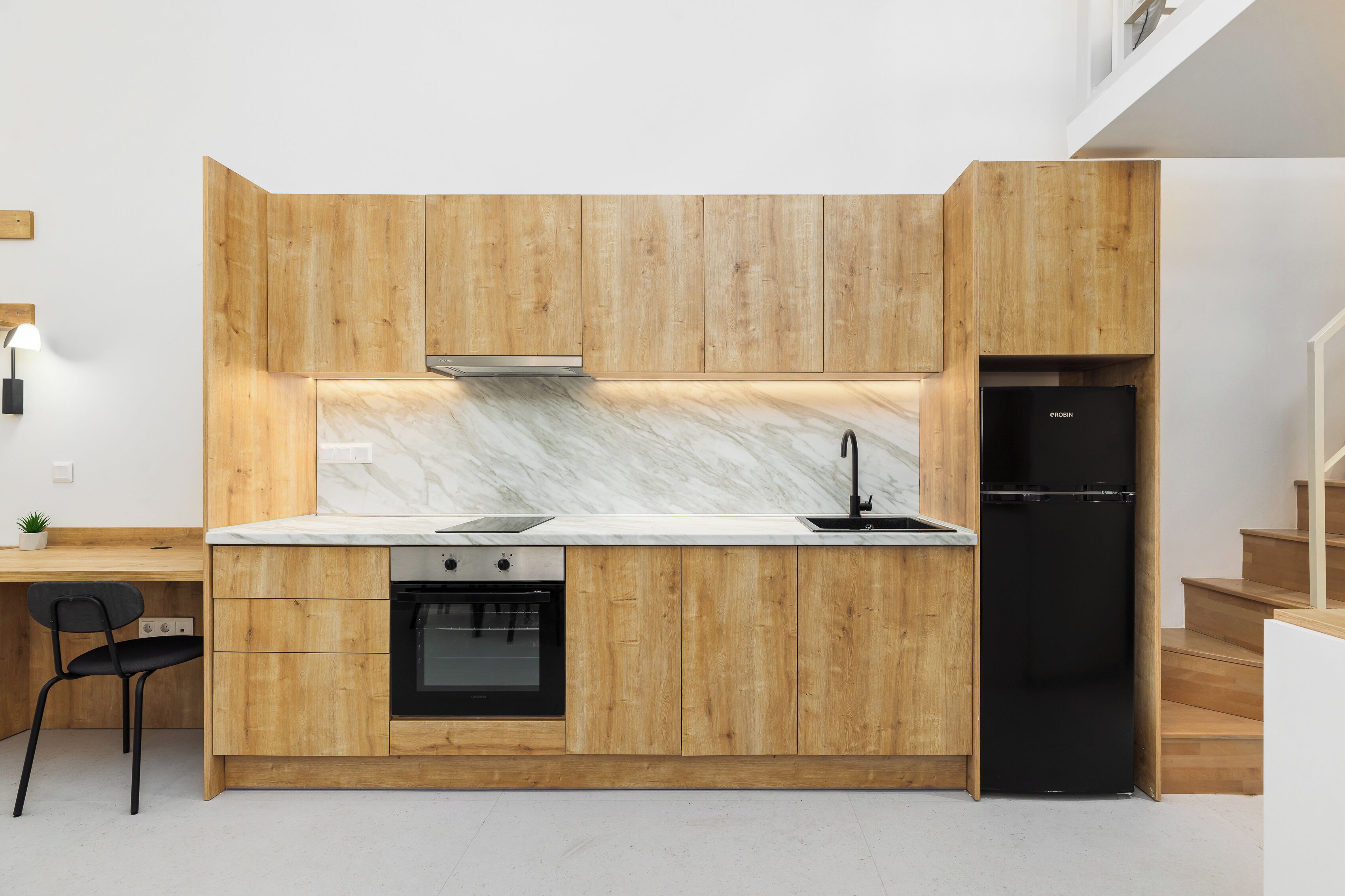 Cocina moderna con armarios de madera, encimera de mármol, refrigerador negro y horno empotrado.