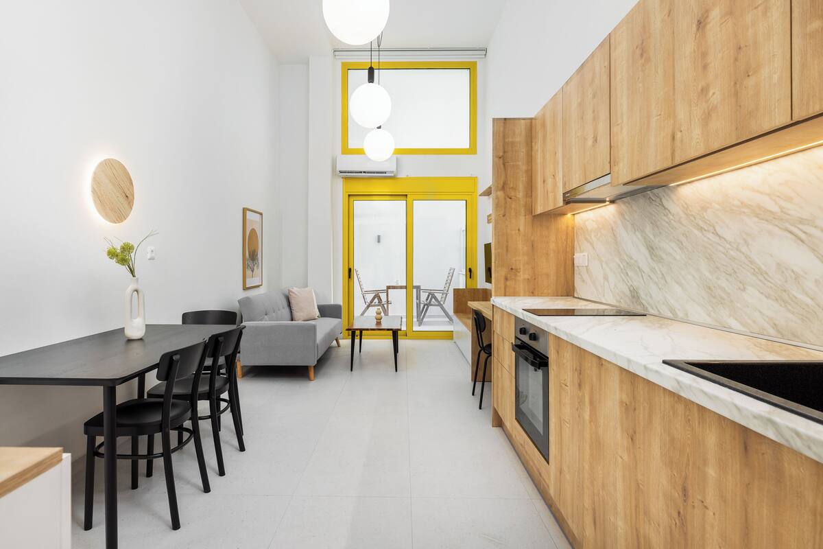 A modern kitchen with wooden cabinets, a marble countertop, and a dining area with a gray sofa and black chairs.