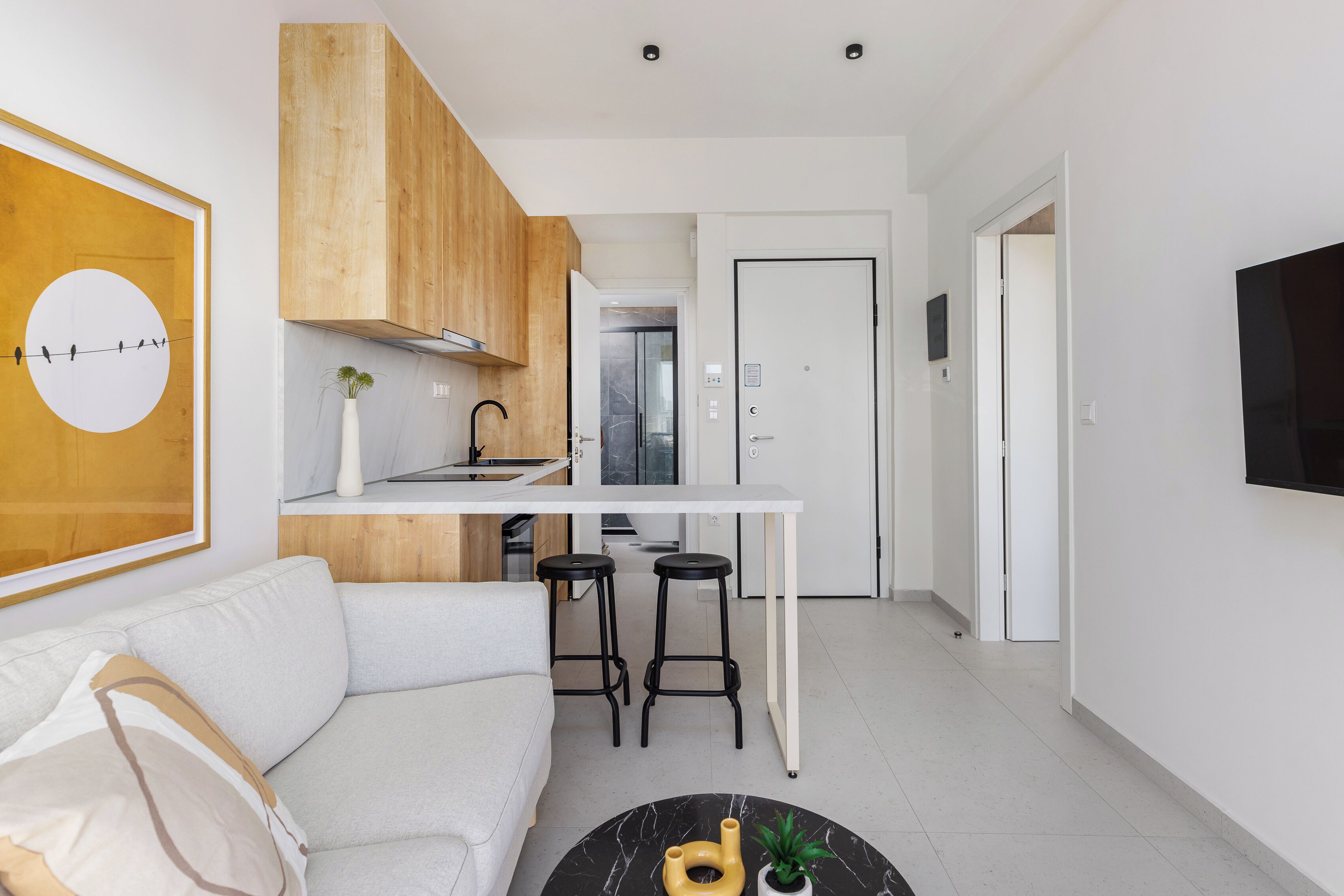 Cozinha moderna com bancada branca, armários de madeira e dois banquinhos pretos.