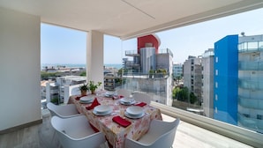 Ein Essbereich mit einem Tisch für vier Personen, große Fenster mit Blick auf die Stadt und ein rotes Gebäude im Hintergrund.