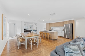 A modern kitchen with a central island, wooden flooring, and a grey sofa in the living area. - Driftwood on Home Beach - Absolute Beachfront (Point Lookout)