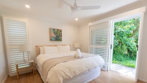 Une chambre à coucher avec un lit, des lampes de chevet, un ventilateur de plafond et une vue sur la verdure par la fenêtre.
