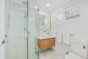 A modern bathroom with a glass-enclosed shower, a wooden vanity, a large mirror, and a toilet with a white tank.