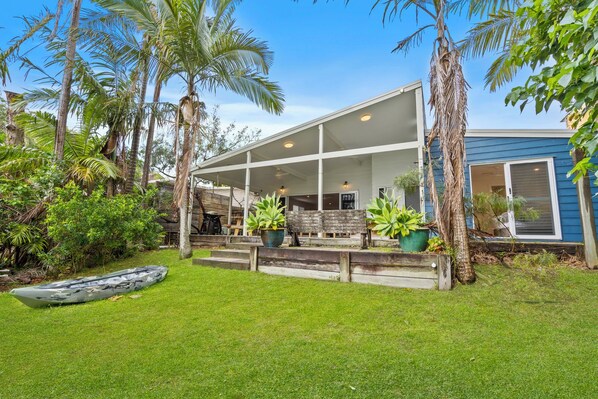 A modern house with a covered porch, surrounded by lush greenery and palm trees.