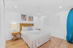 A hotel room with a bed, a bedside table with a lamp, a window with blinds, and two wall art pieces. - Driftwood on Home Beach - Absolute Beachfront (Point Lookout)