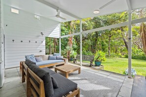 A modern outdoor living space with a sofa, coffee table, and seating area, overlooking a lush garden.