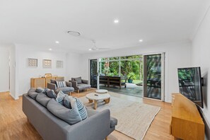 A modern living room with a grey sofa, a coffee table, and a TV on a wooden stand. - Driftwood on Home Beach - Absolute Beachfront (Point Lookout)