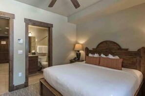 A bedroom with a large bed, a wooden headboard, a nightstand with a lamp, and a bathroom visible through an open door. - Studio-Peak 7 Resort, Hot Tub, Pool, Ski/In/Out! (Breckenridge)