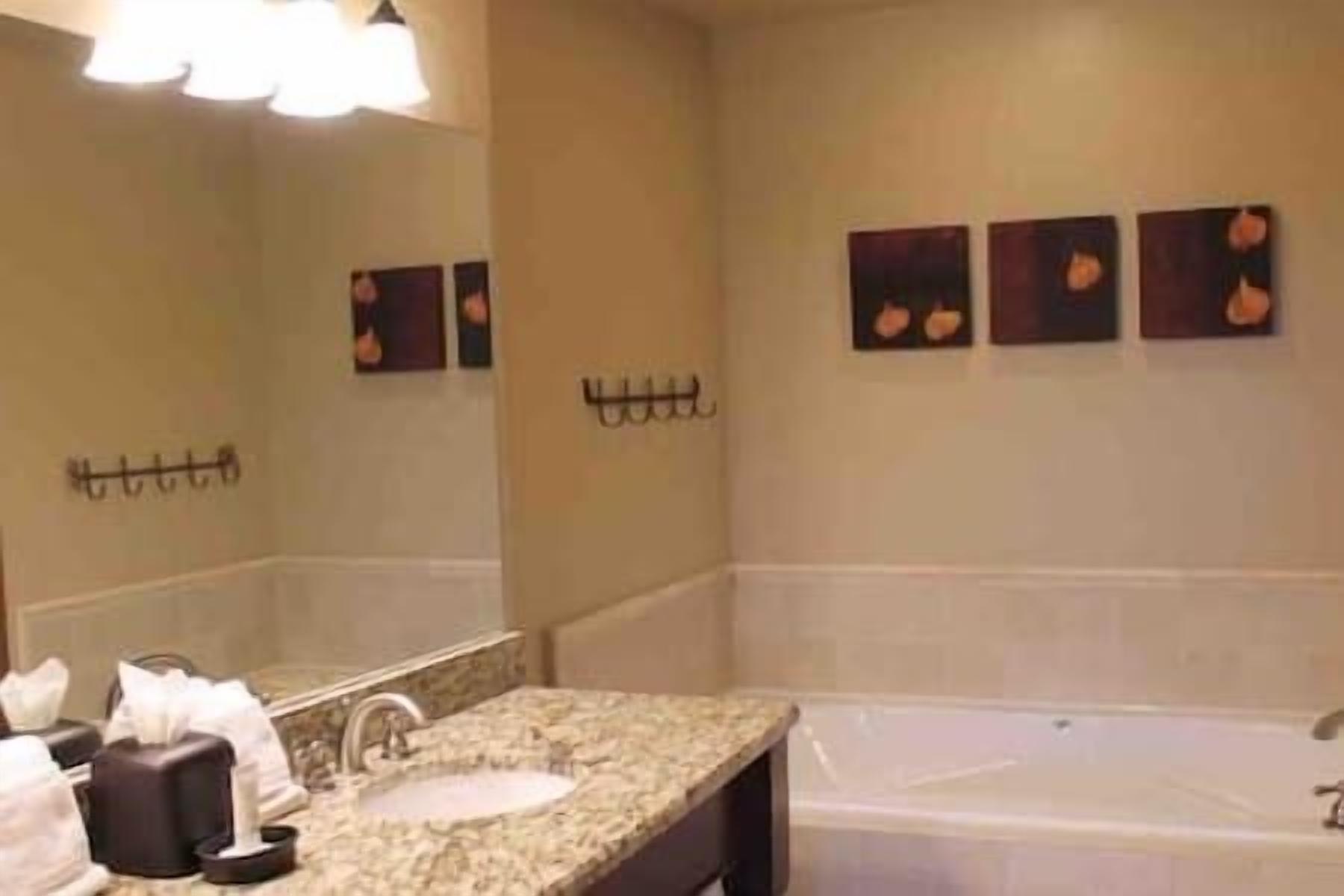 A bathroom with a sink, mirror, and bathtub. There are wall-mounted hooks and three framed pictures on the wall.