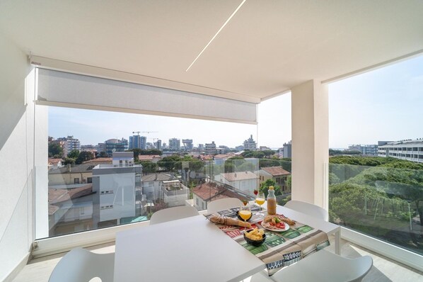 A modern apartment with a balcony, large windows, and a dining area with a table set for two.