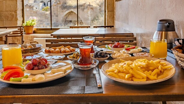 Una mesa con diversos alimentos, como frutas, queso y pan, en una habitación con vistas a edificios antiguos.