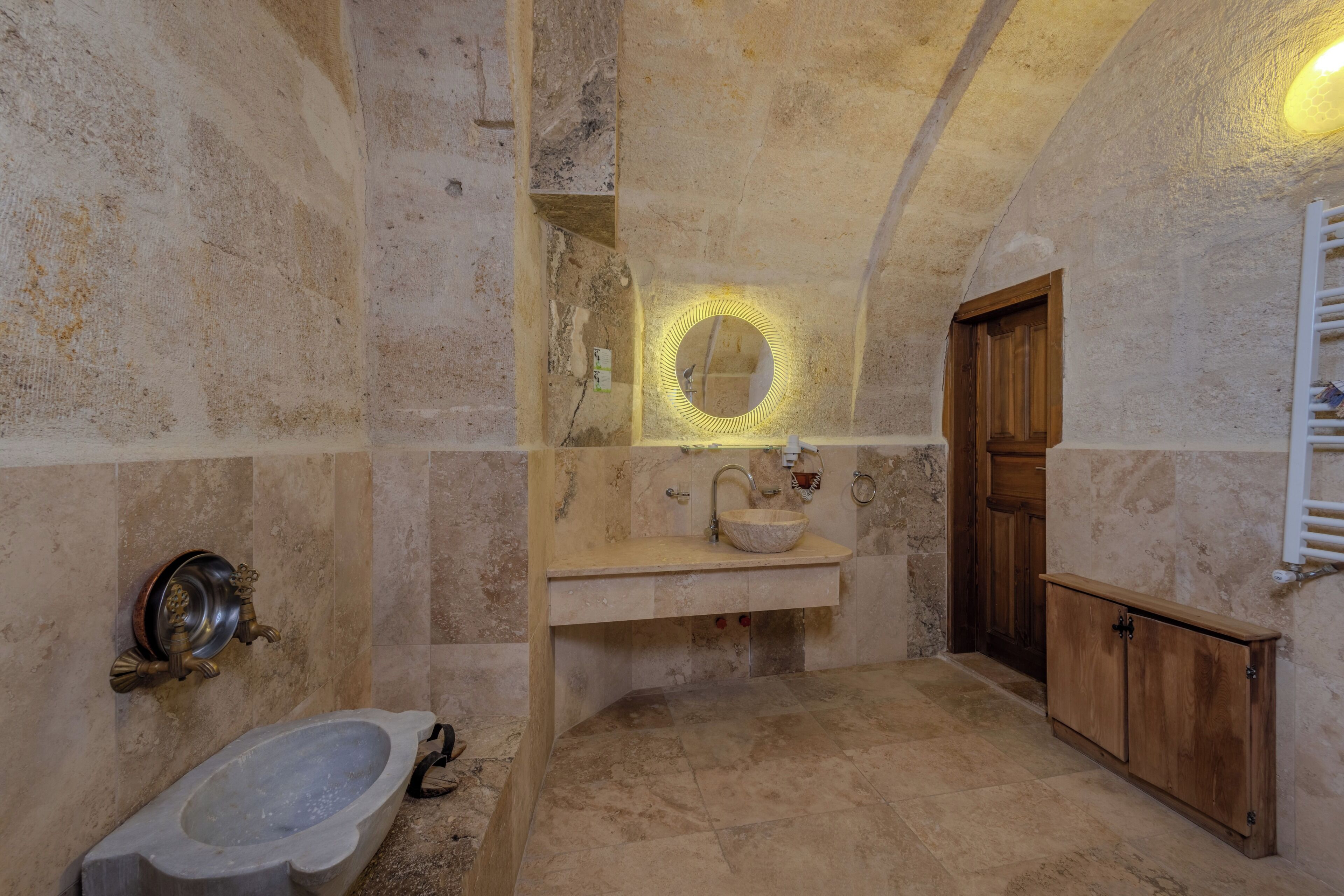 Un baño con un lavabo de piedra, una puerta de madera y un espejo con luz.
