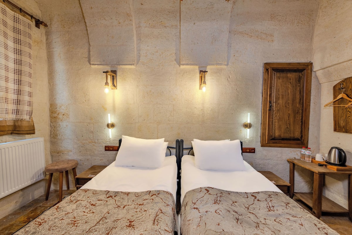 A room with two beds, a wooden table with a kettle, and a radiator.