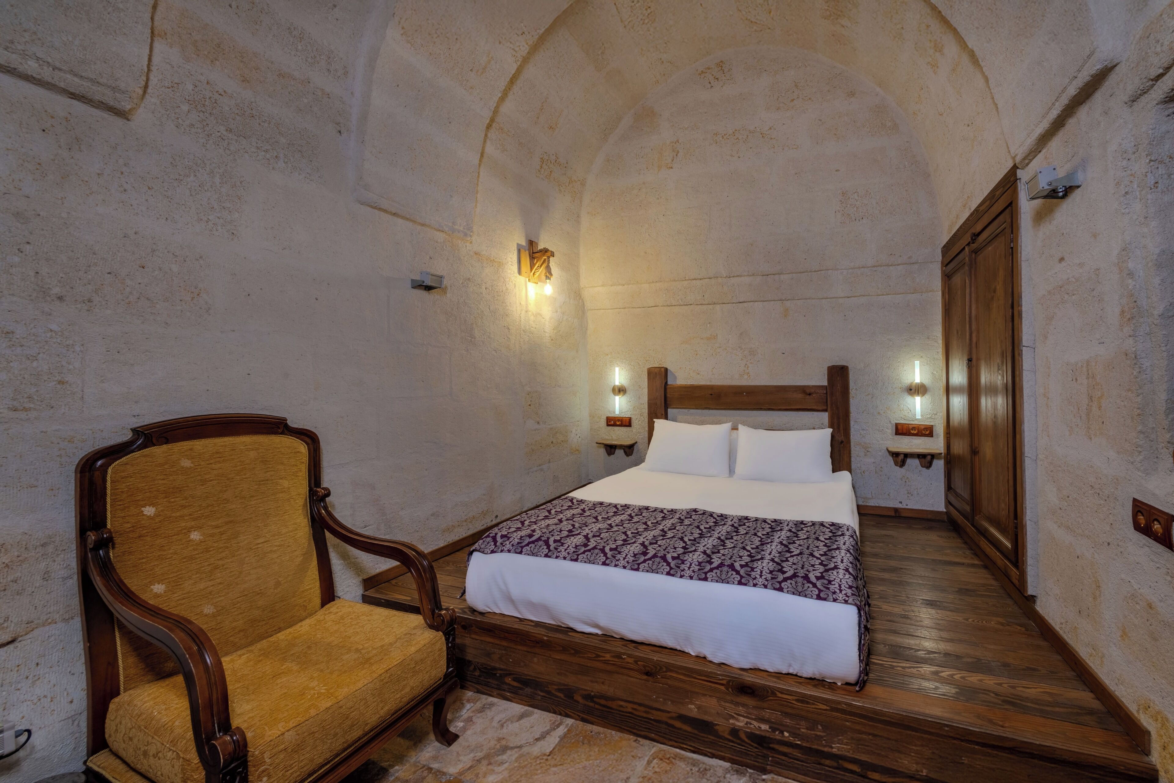 A bedroom with a wooden bed, a chair, and two wall-mounted lights.