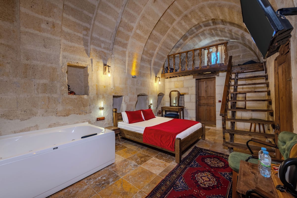 A room with a bed, a wooden ladder, a wooden chair, a small table, and a large bathtub.