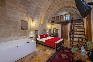 A room with a bed, a wooden ladder, a wooden chair, a small table, and a large bathtub. - Cappadocia Balloon House (Urgup)