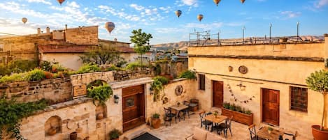 Une cour bordée de murs en pierre, avec des sièges en plein air et des montgolfières dans le ciel.