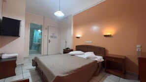 A bedroom with a bed, bedside tables, a TV, and a bathroom door. - Hotel Cosmos (Athens)