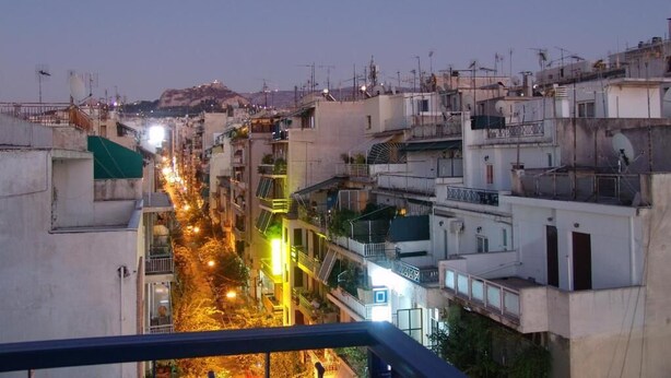 A cityscape at dusk with buildings and a street illuminated by streetlights. - Hotel Cosmos (Athens)