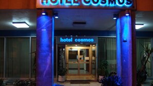 The entrance of Hotel Cosmos with a glass door and illuminated signage. - Hotel Cosmos (Athens)