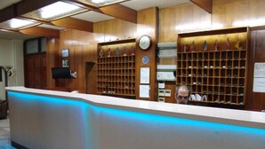 A reception desk with a blue-lit counter, wooden paneling, and a clock on the wall. - Hotel Cosmos (Athens)