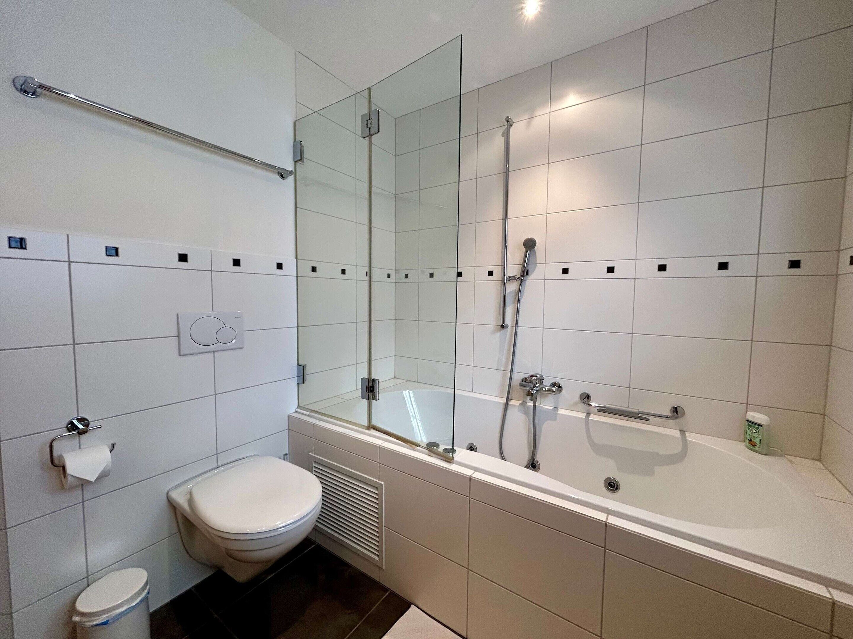 A modern bathroom with a toilet, bidet, and a bathtub with a showerhead.